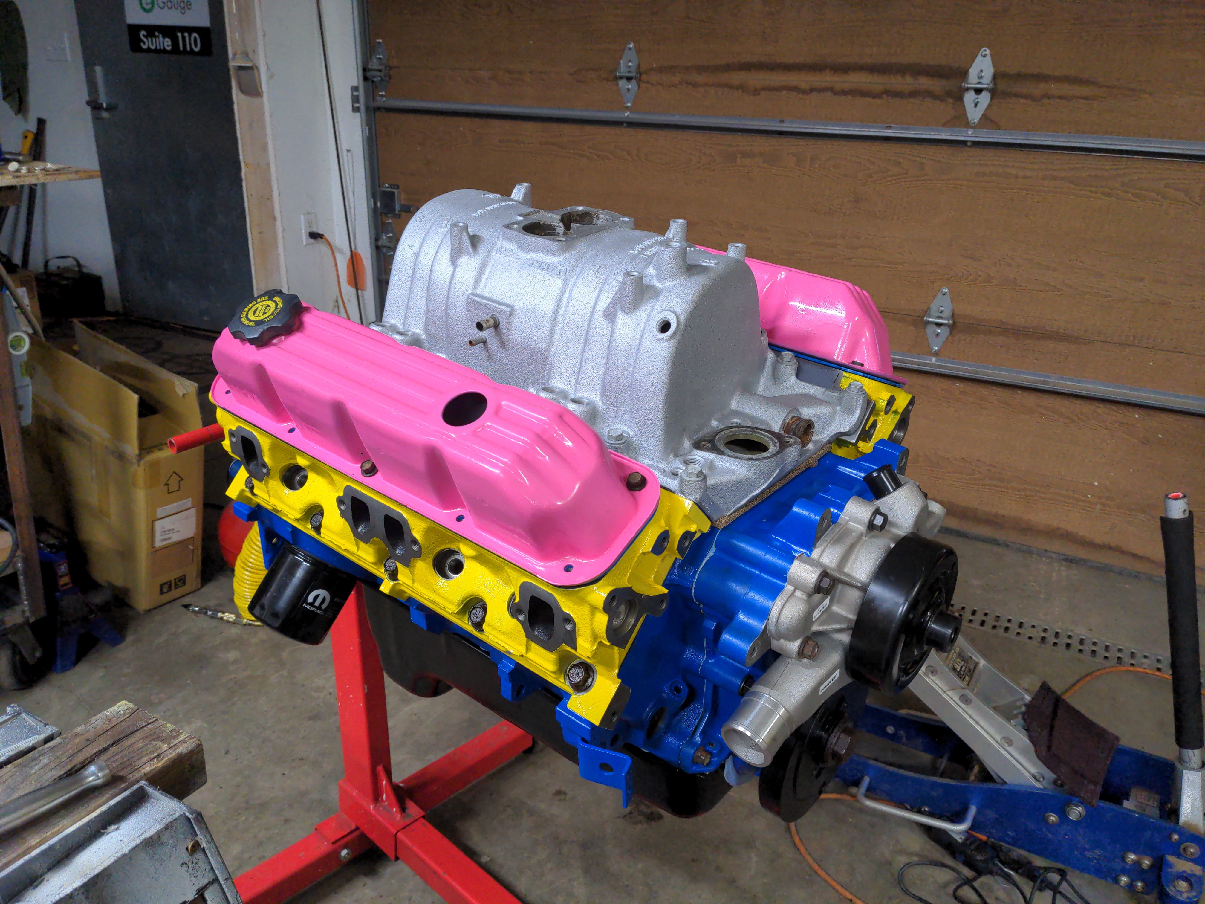 We're finally here; the engine as it stands today. With the blue block, yellow heads, and pink valve covers, the engine is meant to evoke the color scheme of the pansexual pride flag. It's also got a nice silver intake manifold on top; this is painted, but is usually bare aluminum. The accessory brackets will be painted in a similar color.