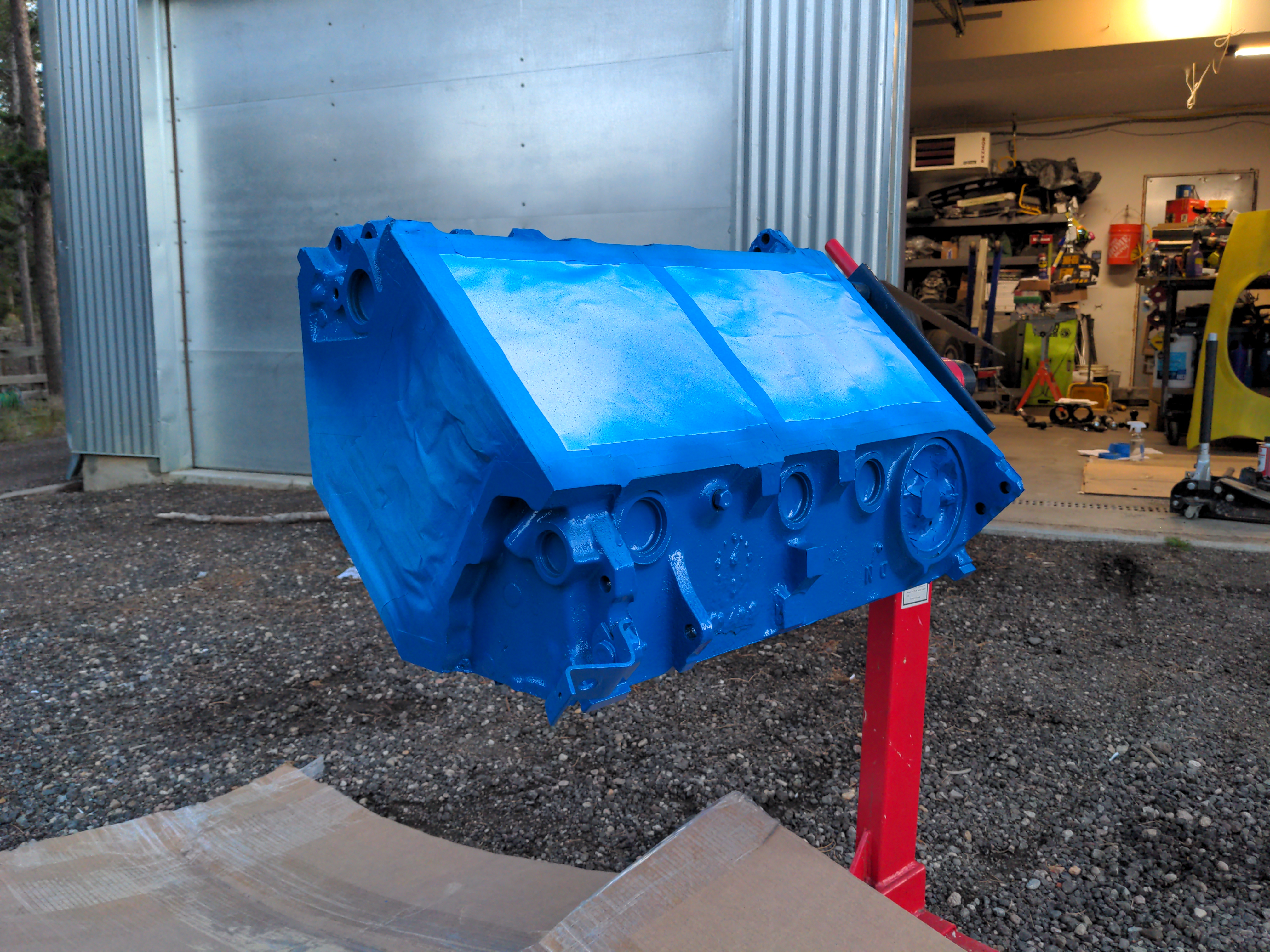 The same V8 engine block (which I'm sure you're tired of hearing about already) on an engine stand outside. The block has had all openings taped off, and it's been painted dark blue with high-temperature engine paint).