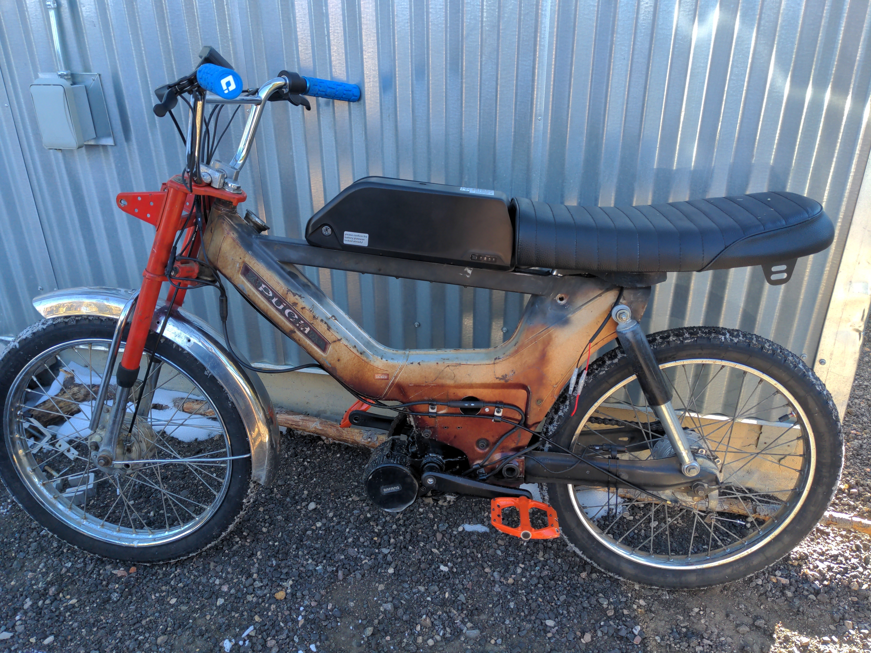 A custom fabricated metal bracket, slotted into the frame of a Puch moped. The bolt holes in the bracket line up nicely with the holes in the frame. The welds are a little rough, but serviceable.