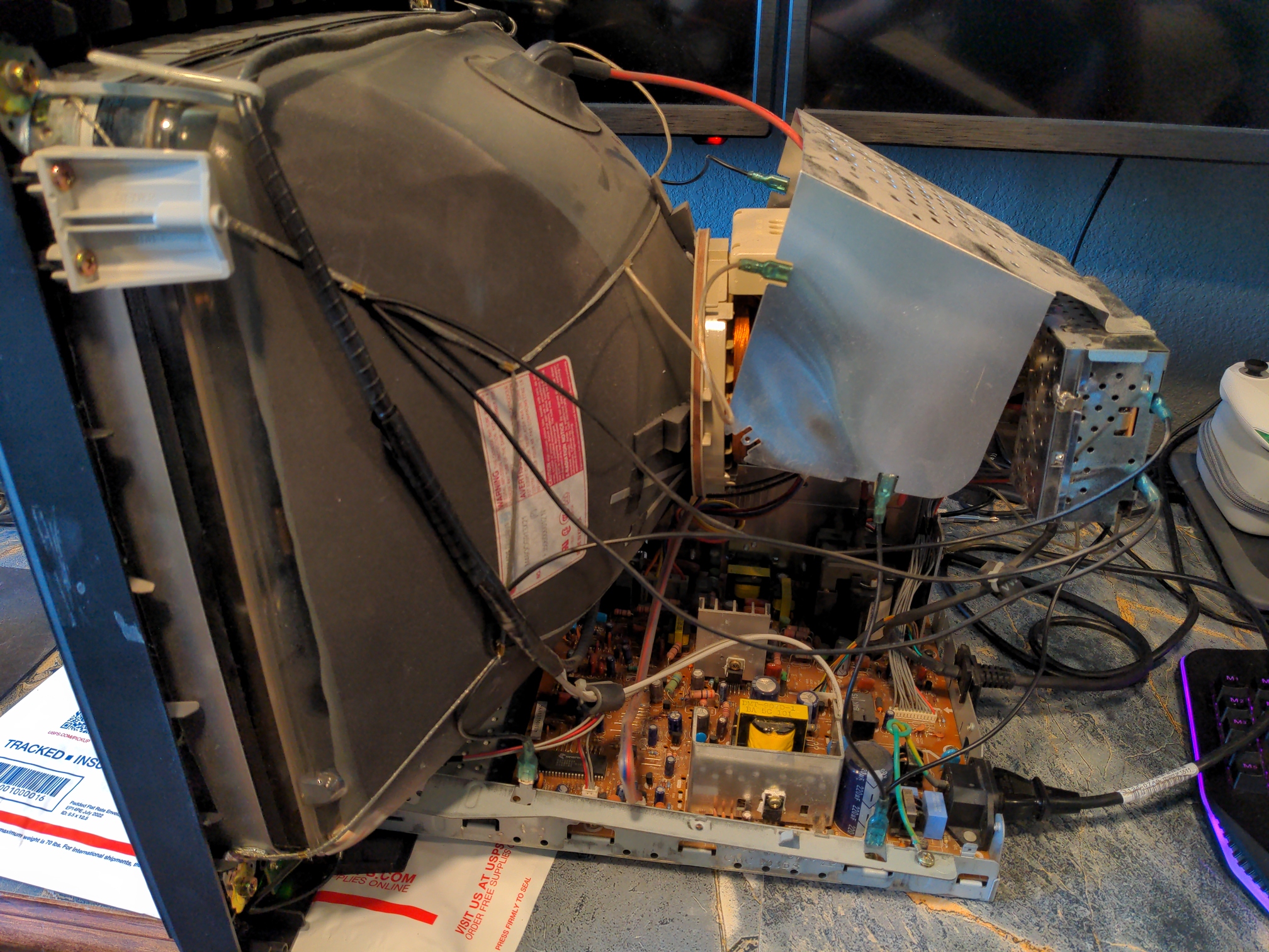 A partially disassembled Insignia monitor. The outer shell has been removed, and the internals are visible. The primary focus is the back of the picture tube and the numerous grounding wires and plates covering the electronics.