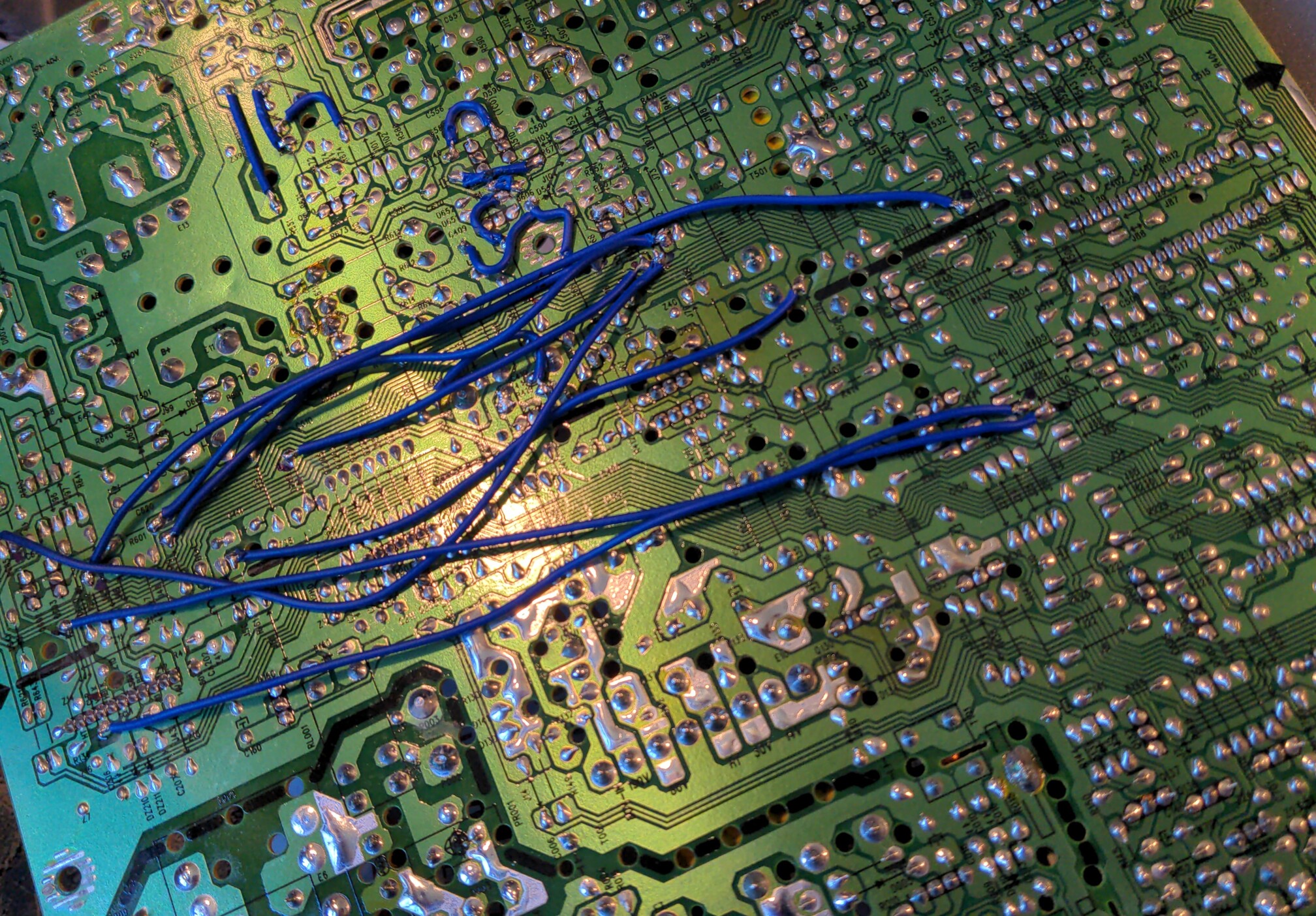 Closeup of a CRT control board, with damage visible around a mounting hole. The board is cracked in three directions radiating out from this mounting hole, with cracks through numerous traces. The board has been repared with numerous small pieces of wire which bypass the damaged areas.