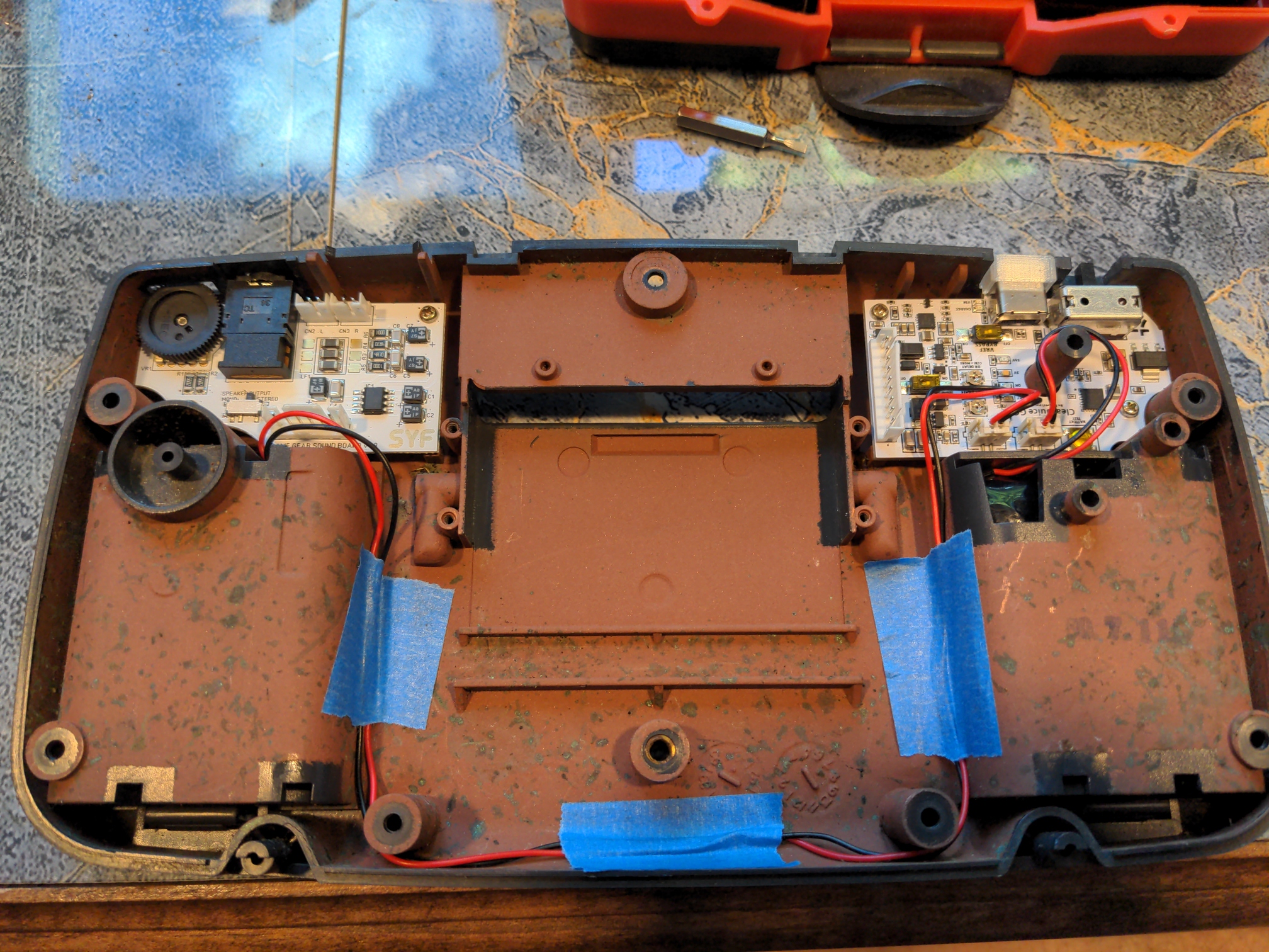 The outer shell of a Sega Game Gear, rotated to show the interior. The main board has been removed, and the secondary boards for audio (left) and power (right) have both been replaced with new components